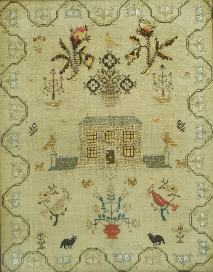 A framed 19th century needlework sampler by Ann Dunham. (undated). Worked with a large floral motif of flowering buds, above a central motif of a house with railings and two columns, with spot motifs below of dogs, peaco